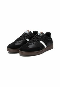Zapatillas negras de cuero y gamuza, con una franja blanca, suela de goma marrón y un logo naranja en la lengüeta.
