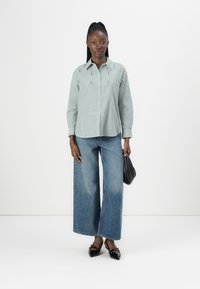 Grön och vit randig skjorta med knäppning och lång ärm, i kombination med vida blå denimjeans och svarta spetsiga skor.