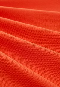 Struktureret orange stof med synligt ribbet mønster, der viser glatte, bløde bølger og folder. Ensartet farve med en konsistent tekstur.