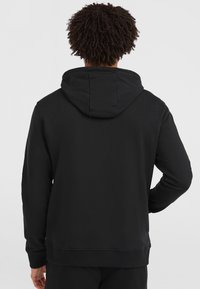 Schwarzer Hoodie mit einer Kordelzugkapuze, gerippten Bündchen und Saum. Glatte Textur, minimalistisches Design, Rückansicht zeigt eine lockere Passform.