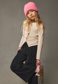 Beiges, geripptes Langarmoberteil, marineblaue, weit geschnittene Hose, pinke Strickmütze und Sneakers mit Animalprint und pinken Akzenten.