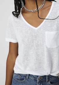 Hvid V-hals T-shirt i let, tekstureret stof med rullede ærmer og en brystlomme, parret med blå denim jeans.
