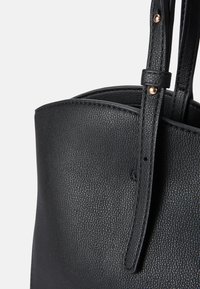 Svart skinn tote bag med teksturert overflate, med en enkelt håndtak og detaljer i messingfarge nær stroppen.