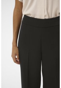 Svarta byxor med hög midja och slät textur, med vidare ben och subtila veck, kombinerade med en ljus, löst sittande topp.