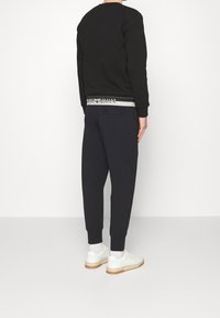 Czarna bluza z okrągłym dekoltem i ściągaczami, zestawiona z granatowymi dresami z pasem w srebrnym logo. Uzupełniona białymi trampkami.