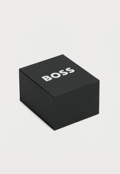 Boîte carrée noire avec le mot « BOSS » imprimé en lettres majuscules blanches sur le dessus, sur un fond clair uni.