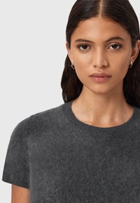 Mørkegrå kortærmet striktrøje med rund halsudskæring. Blød, fluffy tekstur med en tætsiddende silhuet og ribbede manchetter.