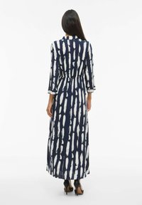 Jūreivio ir baltos spalvos ilgos rankovės suknelė su šepetėlio raštu, suspausta juosmens zonoje ir plaukiojančiu sijonu, papildyta juodais aukštakulniais.