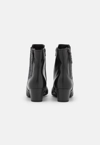 Botas tobilleras de cuero negro con acabado liso, con cremallera lateral y tacón cuadrado modesto. Diseño sencillo con acentos mínimos.