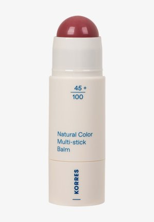 Baume multi-usage couleur naturelle dans un tube blanc avec du baume rouge exposé, étiqueté "45+ / 100" et marqué "KORRES" en texte bleu.