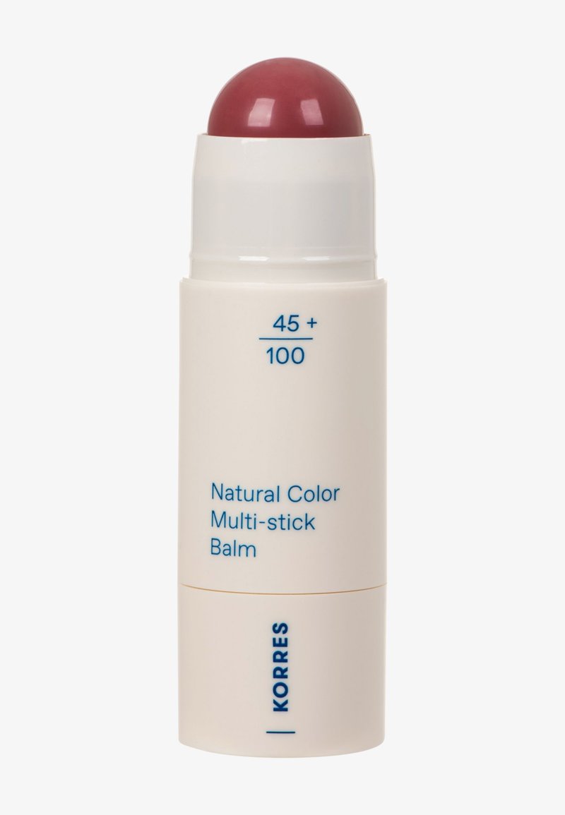 Baume multi-usage couleur naturelle dans un tube blanc avec du baume rouge exposé, étiqueté "45+ / 100" et marqué "KORRES" en texte bleu.