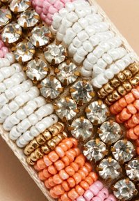Pulsera de cuentas con cuentas rosas, blancas, naranjas y doradas, intercaladas con rhinestones claros en monturas de latón. Superficies lisas y texturizadas.