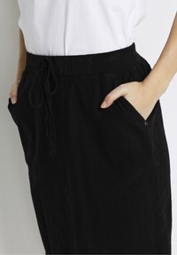 Jupe noire à taille élastique avec cordon de serrage, dotée de poches latérales et d'un tissu doux et texturé. Design simple sans motifs ni accents.