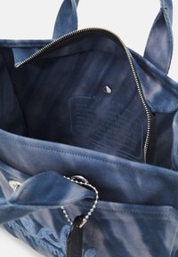 Blauwe stoffen draagtas interieur met ritssluiting, reliëfontwerp en binnenlabel. Voorzien van een zilveren kettingdetail aan de buitenzijde.