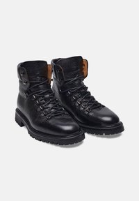 Gli stivali da trekking in pelle nera presentano una finitura testurizzata, occhielli in metallo e accenti in tan contrastante sul colletto, con una suola in gomma robusta.