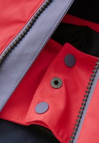 Der rot-graue Außenstoff hat ein Fischgrätmuster. Er verfügt über einen Reißverschluss und Druckknöpfe, mit einer glatten Textur und kontrastierenden Farben.