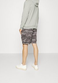 Pantaloni cargo in grigio con motivo mimetico, realizzati in tessuto leggero. Abbinati a un hoodie grigio chiaro e sneakers bianche.