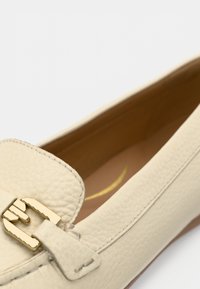 Lichtbeige leren loafers met een gestructureerde afwerking, voorzien van een goudkleurige gesp en gestikte details langs de zijkanten.