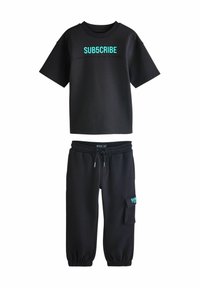 Sort bomulds t-shirt med "SUB5CRIBE" i turkis og sorte sweatpants med elastiske manchetter og sidelommer, begge lavet af blødt materiale.