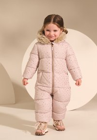 Roza skijaška jakna s punjenjem i zlatnim zvjezdicama, s kapuljačom obloženom krznom, zatvaračem na patent i dva prednja džepa; uparena s bež i ružičastim čizmama.