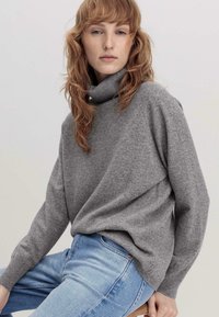 Grijze coltrui van zachte breiwerk, met een ontspannen pasvorm en verlaagde schouders, gecombineerd met lichtblauwe jeans. Minimalistisch ontwerp.