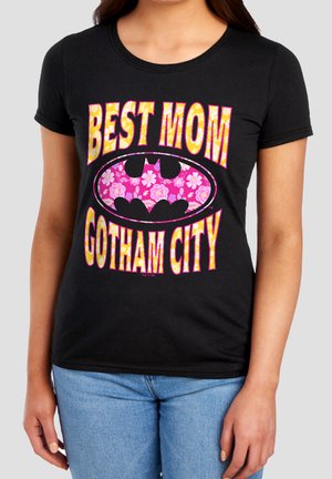 Woman wearing a black T-shirt with yellow and pink text "Best Mom Gotham City" and a floral pink Batman logo in the center.