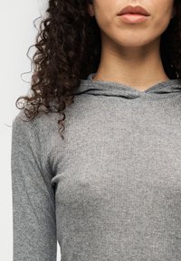 Γκρι μακρυμάνικη μπλούζα με ρίγες και κουκούλα, με απαλό ύφασμα και εφαρμοστή σχεδίαση. Η λαιμόκοψη έχει μία μικρή άνοιξη. Απλή, λειτουργική σχεδίαση.