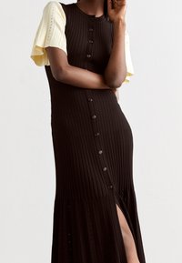 Abito in maglia con un design a coste nere e maniche gialle a contrasto, bottoni sul davanti e spacchi laterali per un tocco in più.
