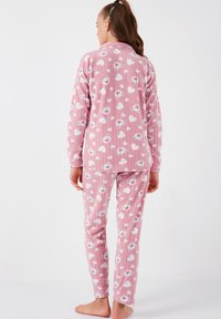 Set de pijama din bumbac roz cu textură striată, având modele repetitive cu urși și inimioare. Tricou cu mânecă lungă și guler, împreună cu pantaloni asortați.