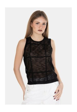 Giovane donna con capelli lisci castano chiaro che indossa un top nero senza maniche in rete e pantaloni bianchi su uno sfondo chiaro uniforme.