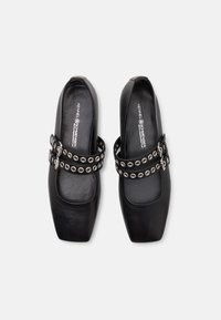 Paire de ballerines noires à bout carré avec double bride ornée d'œillets et boucles argentées, étiquetées Kennel & Schmenger à l'intérieur.