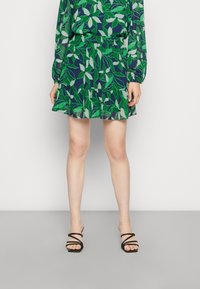 Blusa a motivi fogliari in verde e blu navy, abbinata a una gonna a campana coordinata. La gonna ha un elastico in vita. Indossata con sandali neri con cinturini.