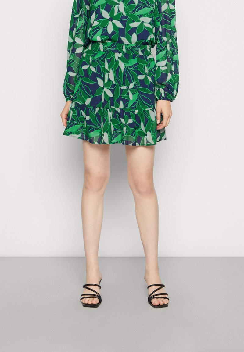 Blusa a motivi fogliari in verde e blu navy, abbinata a una gonna a campana coordinata. La gonna ha un elastico in vita. Indossata con sandali neri con cinturini.