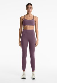 Soutien-gorge de sport violet et leggings taille haute en matériau lisse et extensible. Équipé de bretelles réglables et de chevilles fuselées.