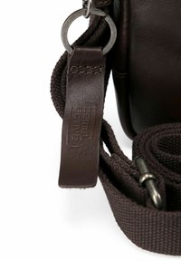 Correa de bolsa de cuero marrón con textil trenzado y herrajes de metal. Presenta una etiqueta grabada en el accesorio de cuero.