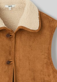 Veste sans manches en suédine marron avec un col en shearling beige, dotée de deux boutons marron. Texture douce et finition lisse.