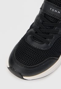 Scarpa da ginnastica nera con tomaia in mesh, lacci e colletto imbottito. La suola è bianca con una sezione nera testurizzata sulla punta.