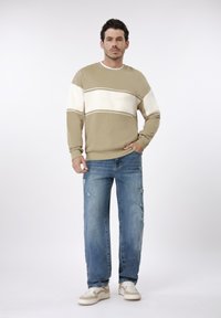 Μπεζ πουλόβερ με ρίγες σε λευκό και ταμπά, συνδυασμένο με ανοιχτό μπλε τζιν με φθορές. Τα παπούτσια έχουν μπεζ και λευκές λεπτομέρειες.