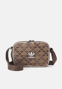 Brązowa torba o wzorze w kształcie prostokąta, z regulowanym paskiem i białym logo Adidas z przodu. Teksturowany materiał z gładkim wykończeniem.