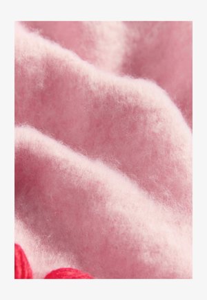 Rózsaszín gyapjú anyag puha, bolyhos textúrával és lágy hullámokkal. Kiemelkedő részletek közé tartozik a piros fonal díszítés a széleken.