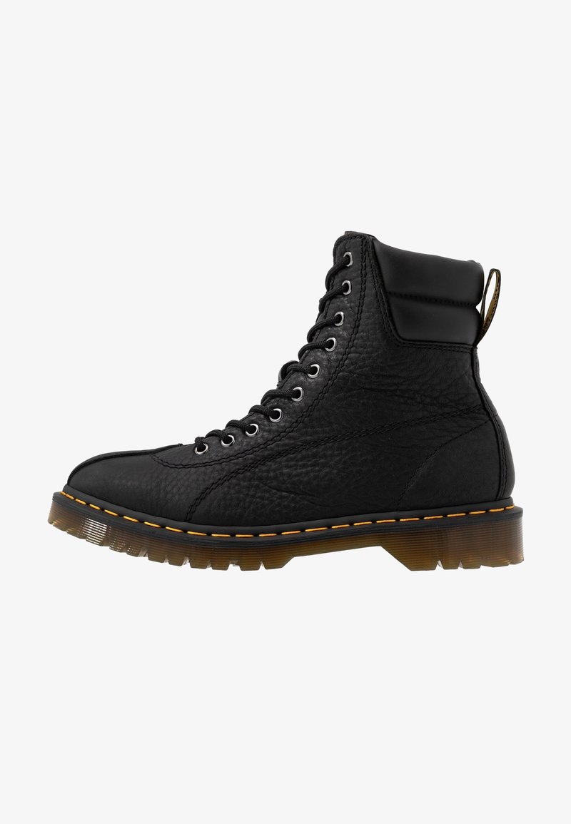 Botte montante en cuir noir avec semelle épaisse à crampons marron, couture jaune, neuf œillets avec lacets noirs et col rembourré autour de la cheville.
