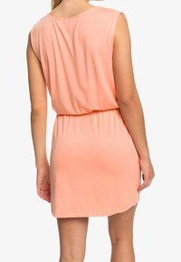 Robe sans manches de couleur pêche avec une coupe décontractée, taille élastique et texture de tissu douce. Design simple et longueur mi-cuisse.