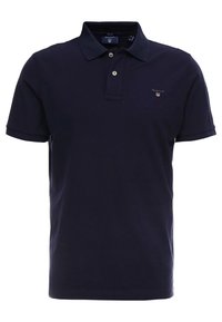 Marinblå pikétröja i bomull med klassisk krage, korta ärmar och en liten broderad logotyp på bröstet. Designen är enkel och ren.