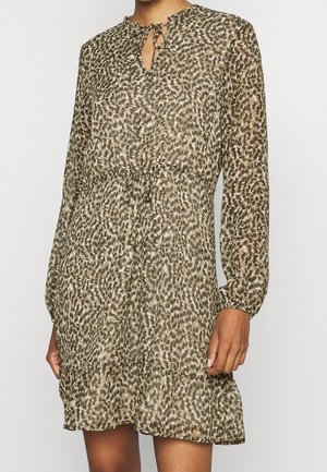 Kvinde iført en langærmet, knælængde kjole med et abstrakt brunt og beige mønster og bindebånd ved halsudskæringen.