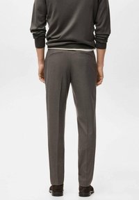 Pantaloni da abito grigi a vestibilità slim con due tasche posteriori, superficie liscia e dettaglio di piega. Indossati con un maglione scuro, che mostra un design moderno.