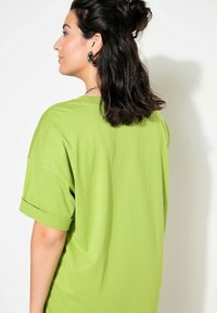 Grøn oversized T-shirt med korte oprullede ærmer og en blød tekstur, rund hals og afslappet pasform.