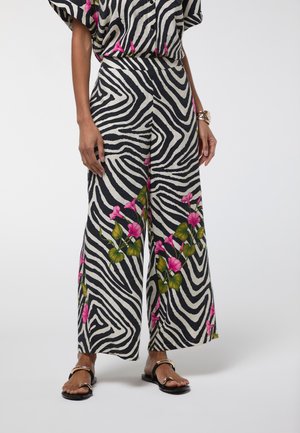 Pantalones de pierna ancha con rayas de cebra en blanco y negro y detalles florales en rosa, combinados con sandalias negras y una pulsera dorada.