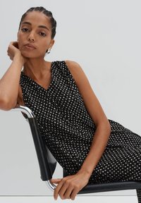Schwarzes ärmelloses Kleid mit V-Ausschnitt-Design, das ein weißes geometrisches Muster aufweist, aus weichem Stoff gefertigt ist und einen lässigen Schnitt hat.