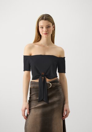 Haut noir à épaules nues avec des manches courtes, texture côtelée, détail à nouer sur le devant, associé à une jupe en denim marron avec une ceinture.