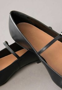 Bailarinas de cuero negro con punta redondeada, que cuentan con una delgada correa en el empeine y una plantilla de color marrón suave. Diseño minimalista.